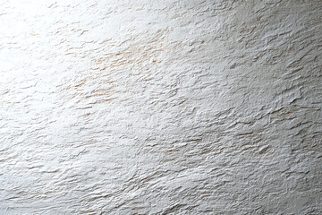 Close-up of a rough, textured white plaster wall with uneven surface patterns and subtle shadows.