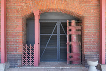 A sturdy industrial-style metal door set in a red brick wall. The design features rivets and...