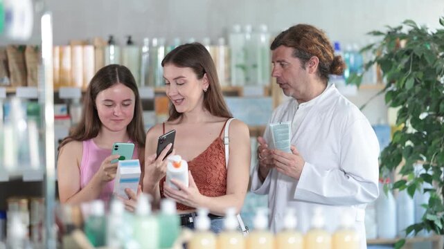 Mother and daughter scan QR code on skin cream packaging at drugstore. Male pharmacist offers to buy skin cream. High quality 4k footage