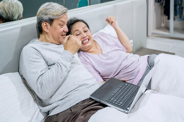 Happy Senior Couple Celebrating Success While Using a Laptop in Bed