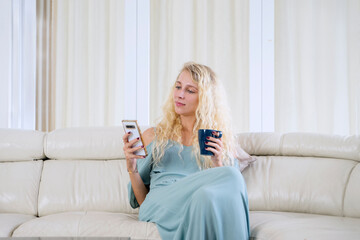 Smiling Woman Holding a Mobile Phone and a Mug on a Couch