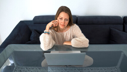 The student looks at the laptop screen. A woman is sitting at a desk with a personal computer in front of her. A lady watching a movie