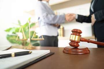 Legal Agreement. Two lawyers shaking hands with gavel and scales in foreground.