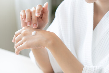Health care, beauty smile pretty asian young woman in bathrobe, towel after shower bath at home, finger applying moisturizer on her back hand. Skin body cream moisturizing lotion, routine in morning.