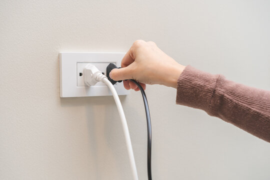 Hand of woman plugged in, unplugged electricity cord cable at home, put on or remove electric plug cable in socket on wall outlet for saving, control power electrical energy, eco environment concept.