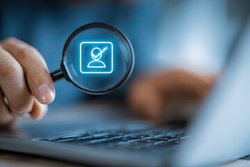 A person using a magnifying glass to focus on a glowing profile icon with a checkmark, likely part of a digital verification or identification process, in front of a laptop