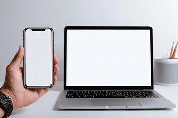 A hand holds a phone next to a laptop, both with blank screens