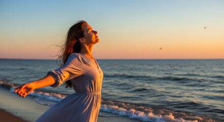 Obraz premium A woman in a dress standing on a beach at sunset, with her arms outstretched.