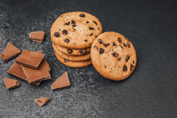 Delicious chocolate chip cookies and chocolate pieces on dark stone surface