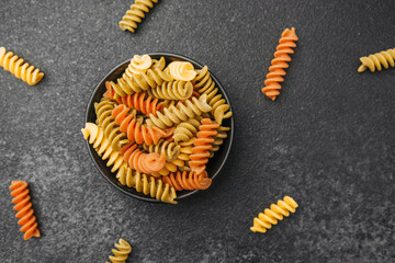 Colorful fusilli pasta in a bowl on a dark textured surface
