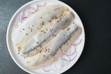 Marinated herring fillets with coriander seeds and onion on white plate over dark background