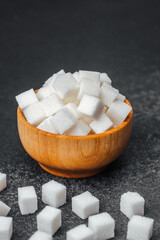 White sugar cubes in a wooden bowl on a dark surface create a simple still life