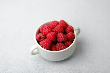 Raspberries in white bowl on light surface for organic food or vegan diet concept