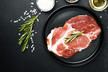 Raw beef steak with herbs and seasonings on black plate