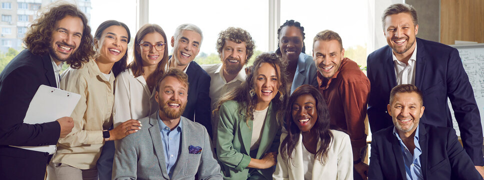 Happy team at business event or work meeting in office. Group portrait of cheerful diverse young and mature people smiling and looking at camera all together. Banner. Business concept