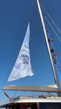 White sailboat sail with the pun 'IDEALLY YOU WOULD SEA WHERE TO GO' against a clear blue sky in Durr&euml;s. Playful navigation & discovery message.