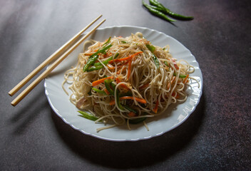 Chinese delicacy hakka noodles served in a plate with chopsticks. Selective focus.