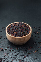Black rice in wooden bowl surrounded by scattered grains