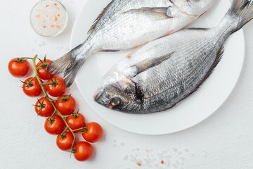 Close up of two dorado fish on white plate with lemon and tomato