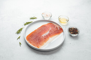 Prosciutto slices on white plate with rosemary and salt