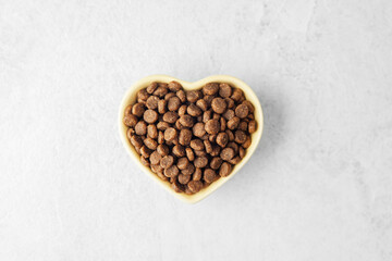 Heart shaped bowl filled with dry dog food on light gray background