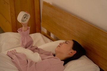 深夜に布団の中で時計を見ている女性