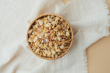 Granola in wooden bowl on soft white textile top view