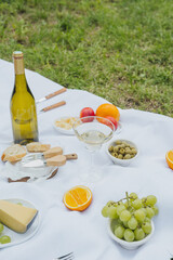 Full picnic setup with wine, cheese and fruits on white blanket for concepts of dining, relaxation and organic lifestyle
