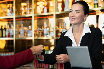 Attractive saleswoman, cashier holding credit card reader serving customers and holding credit card at a retail store counter or bar restaurant counter.	