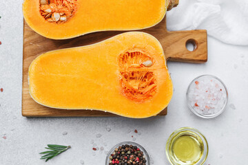 Halved butternut squash on a wooden board with salt, peppercorns, oil and rosemary