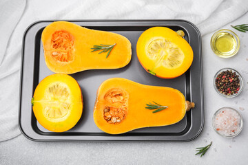 Butternut squash halves with rosemary on baking sheet, oil, peppercorns and salt.