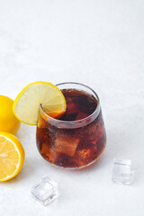 Dark soda with lemon slice and ice cubes served in glass on bright background with citrus garnish