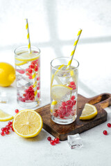 Two tall glasses with lemon red currant water and yellow striped straws on white table
