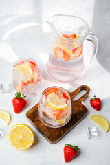 Strawberry lemon infused water in pitcher and glasses served with ice cubes and fresh fruit