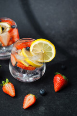 Sparkling lemonade with lemon slices strawberries and blueberries in glass on dark background with fresh fruits nearby