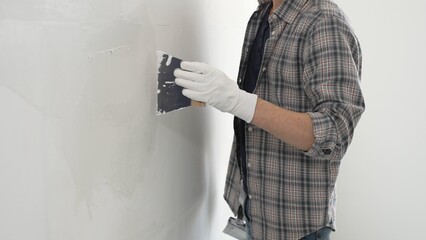 Unknown construction worker man wearing gloves and plaid shirt is using a putty knife to apply...