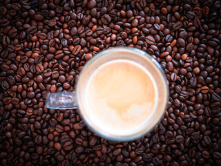 Top view of espresso in glass cup on roasted coffee beans. Morning caffeine drink symbolizing energy, wake up, relaxation and daily routine.