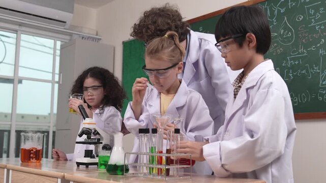 Caucasian boy drop chemical solution in example while diverse student doing experiment. American girl inspect colored liquid while standing with teacher looking after children at blackboard. Pedagogy.