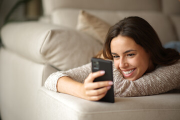 Happy woman checking smart phone lying on sofa