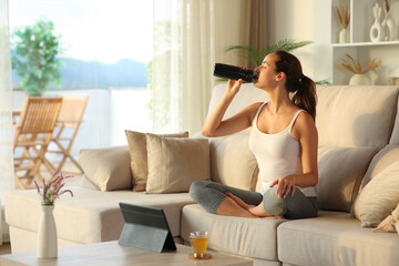 Yogi at home drinking water from bottle during yoga online class