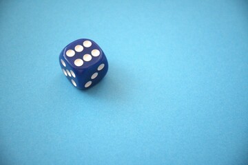 A blue die showing six dots placed on a blue background with copy space, representing luck or gaming.