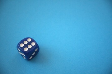 A blue die showing six dots placed on a blue background with copy space, representing luck or gaming.