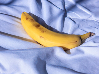 Ripe banana resting on soft, light blue bedding, contrasting bright yellow against muted pastel surface, highlighting minimalist stillness