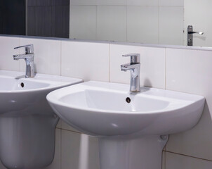 White ceramic sinks flanking sleek chrome faucets, reflecting contemporary bathroom design in polished mirror backdrop, highlighting clean minimalist aesthetic