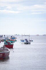 A red long-tail boat floating on calm seawater under a partly cloudy sky, with distant islands on the horizon, capturing the peaceful simplicity of coastal fisherman life