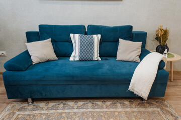 This elegant teal sofa, complete with soft, plush cushions and a cozy throw, perfectly complements a modern living room setting, adding a touch of style and comfort to your home