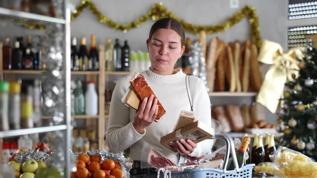 Cheerful young girl standing with shopping basket in grocery shop, surrounded by holiday decorations, holding packages of sweet nutty turron, choosing traditional Spanish desserts for Christmas feast