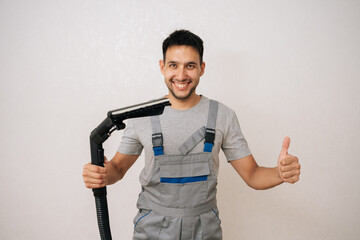 Portrait of cheerful professional cleaning service employee in overall holding washing vacuum cleaner, getting ready to cleaning in living room, smiling looking at camera, showing thumbs up gesture.