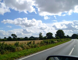 Country road scene with fluffy clouds and green fields
