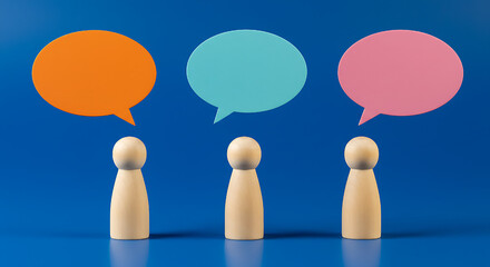 Three wooden figures stand beneath vibrant speech bubbles against a blue backdrop, symbolizing collaborative discussions and communication, ideas